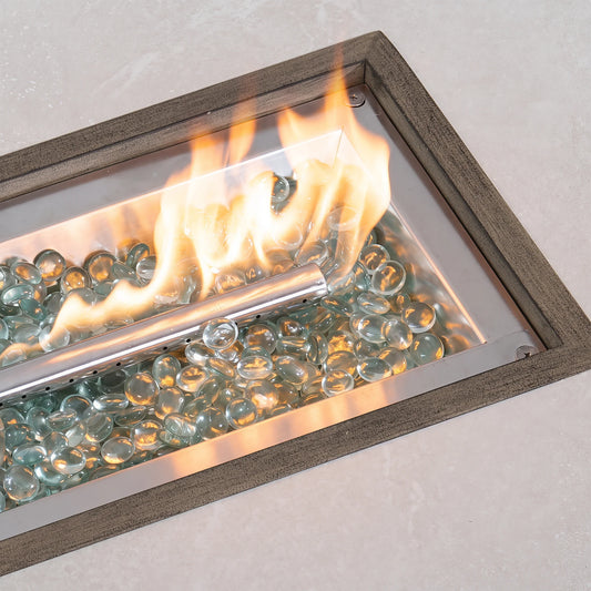 Close-up of dancing flames from a linear stainless steel burner filled with reflective clear fire glass beads inside a gas fire table.