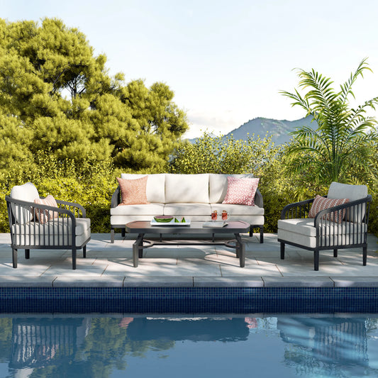 Outdoor patio set with sofa, chairs, and table by a pool with greenery and mountains in the background.