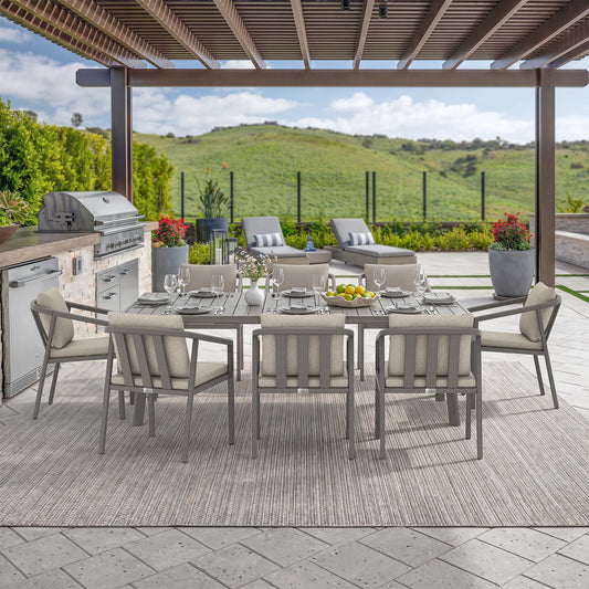 Outdoor dining set on a covered patio with a rectangular gray table, eight matching cushioned chairs and a view of rolling green hills in the background.