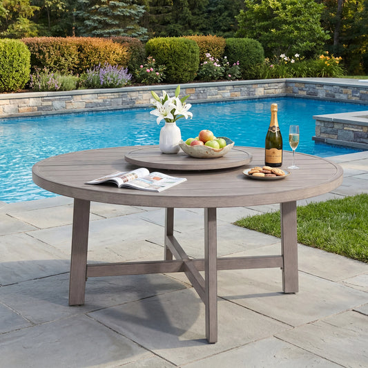 Round wooden outdoor table with a bottle of champagne, fruit, and flowers by a pool.