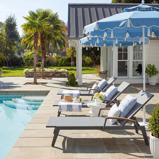 Outdoor patio with lounge chairs, table, and umbrella by a poolside.