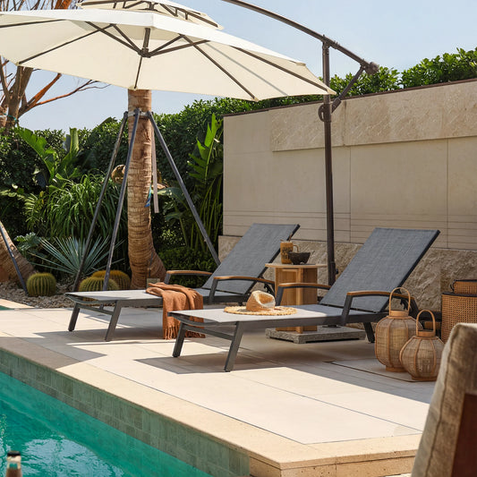 Two lounge chairs under an umbrella by a pool with decorative items on a patio.