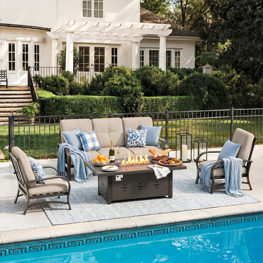 Outdoor patio set with fire pit table by a poolside, featuring chairs, tables, and decorative items.