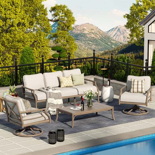 Outdoor seating group consisting of a sofa, two club chairs, and a coffee table with cushions, placed on a patio beside a pool with a mountainous landscape in the background.