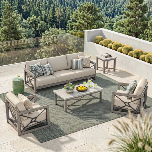 Outdoor patio furniture set arranged on a stone terrace with a forest backdrop, including a beige sofa, two matching armchairs, a rectangular coffee table, a side table, and a green side stool on a gray rug.
