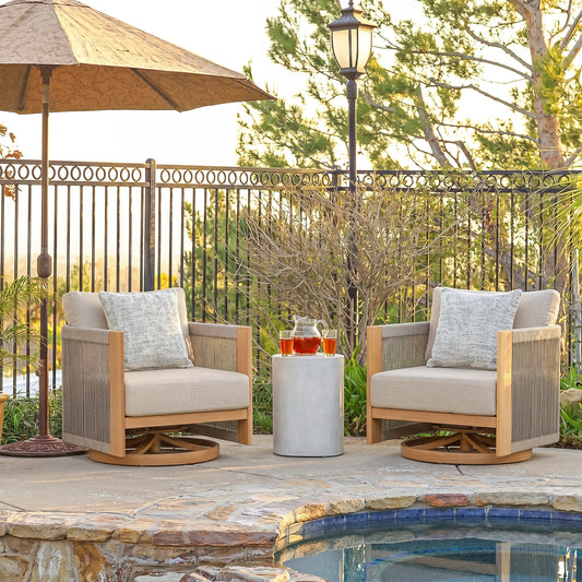 Two wooden chairs with beige cushions and a small table by a poolside, with an umbrella and lamp in the background.