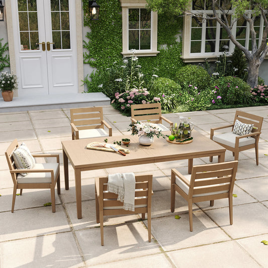 Alcudia 7-piece stationary patio dining set displaying a grand wood-look table and six classic four-leg metal armchairs with thick beige cushions.