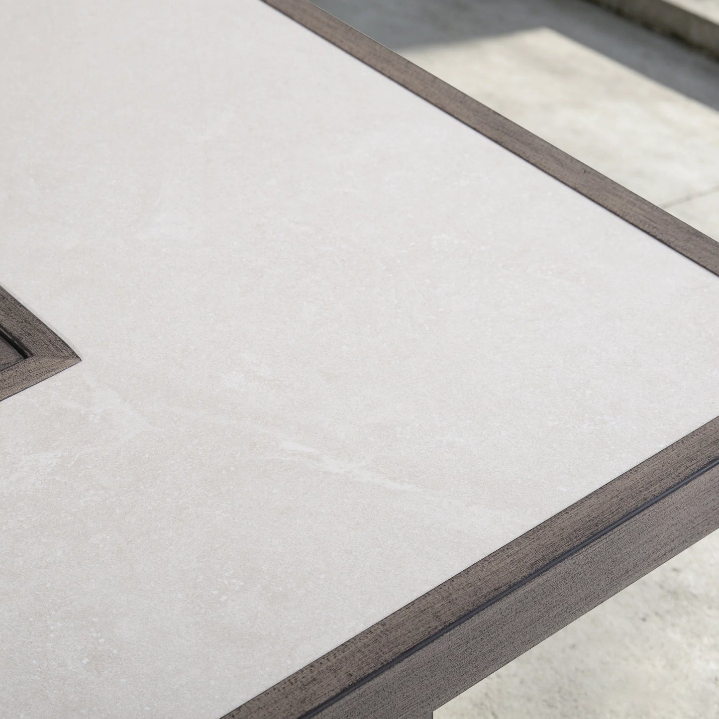 Close-up of the beige ceramic tile tabletop with a textured faux-stone finish, framed by a durable aluminum edge on a patio fire table.