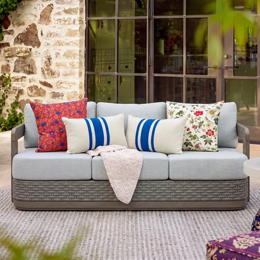 Full front view of the Manarola curved grey outdoor lounge sofa arranged against a rustic stone wall backdrop in a beautiful courtyard setting.