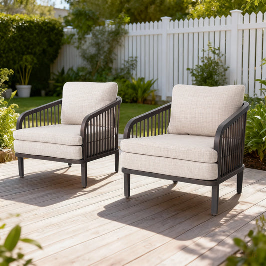 Two outdoor chairs with beige cushions on a wooden deck, surrounded by greenery and a white fence.