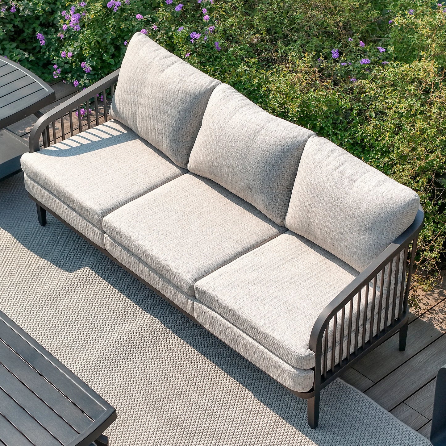 Gray outdoor sofa on a wooden deck with greenery in the background