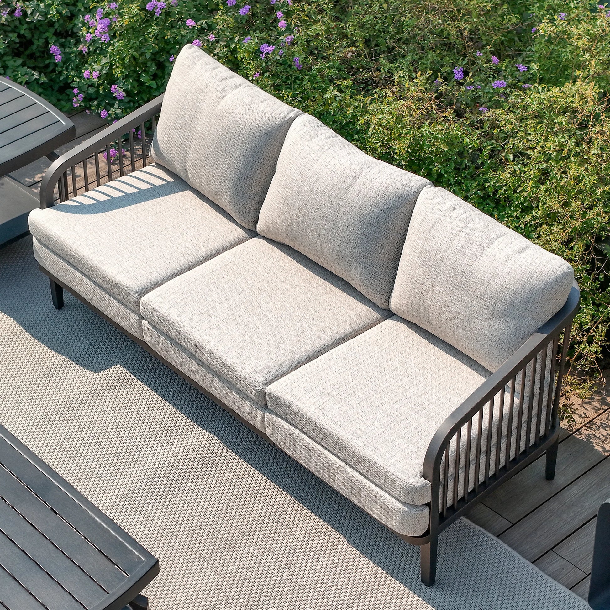 Gray outdoor sofa on a wooden deck with greenery in the background