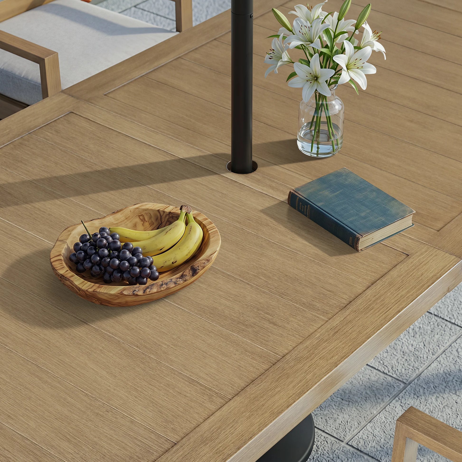 Top-down angled view of the Alcudia outdoor table with a patio umbrella pole installed in the center hole next to a fruit bowl.