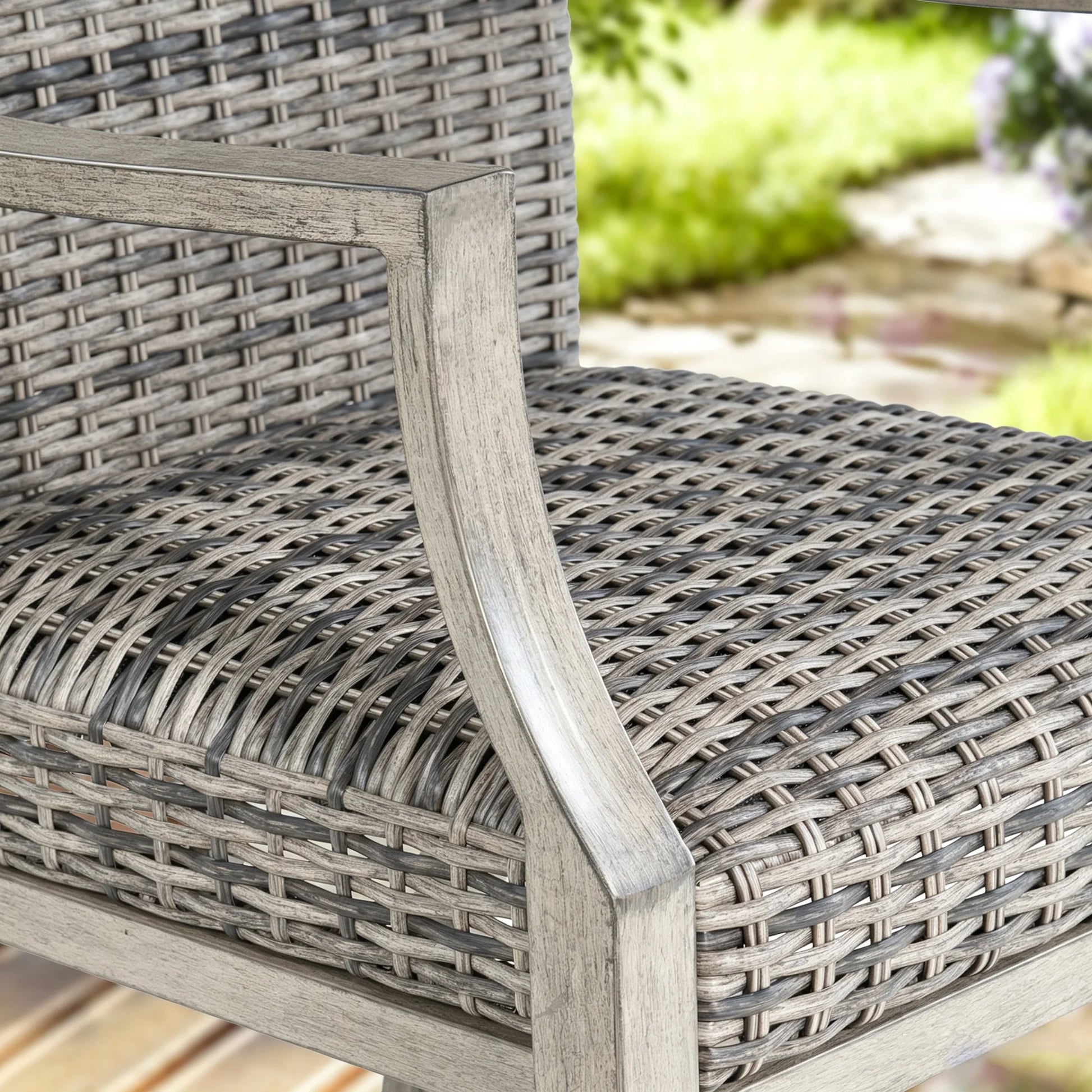 Close-up of a woven patio chair with a weathered gray steel frame and textured seat, overlaid with text reading 'Powder Coated Steel Frame' and feature badges 'Weathered Teak Look', 'Rust Proof', and 'Durable'.