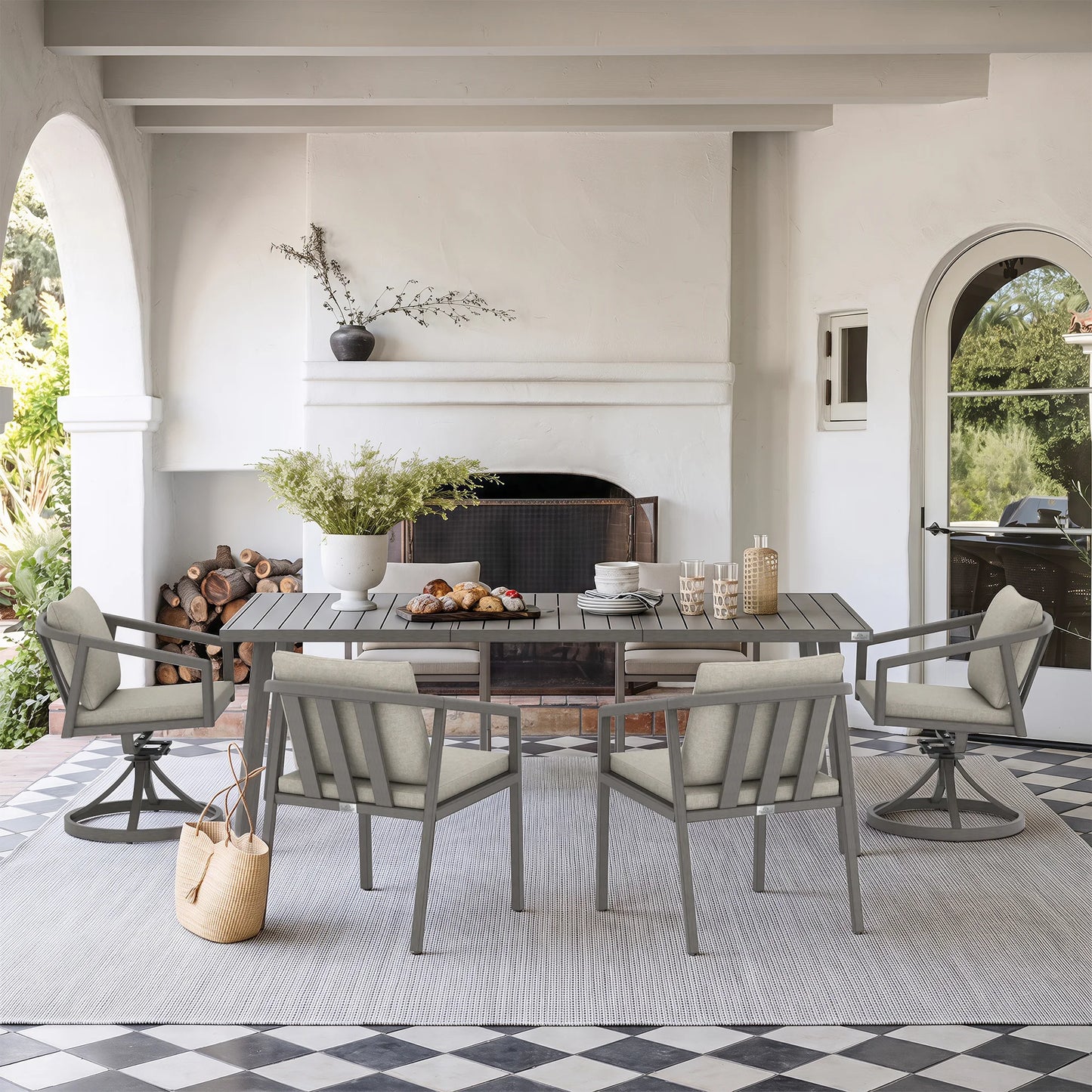 A dining set consisting of a rectangular gray wood-look table and four matching swivel chairs with light beige cushions, arranged on a light gray rug in a bright, modern patio dining room.
