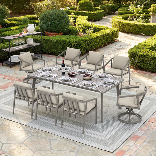 An 9-piece outdoor patio dining set with a rectangular metal table and six cushioned chairs, arranged on a striped area rug in a landscaped garden patio setting.