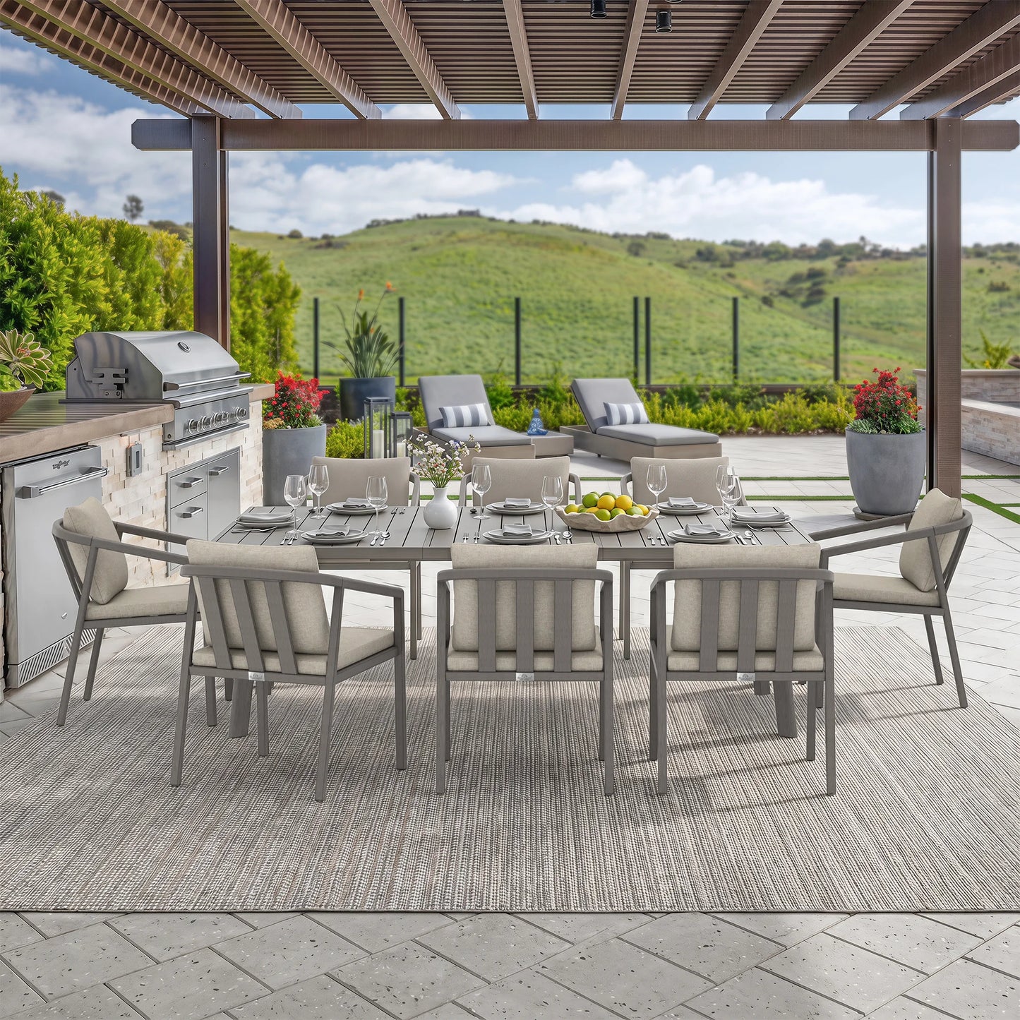Outdoor dining set on a covered patio with a rectangular gray table, eight matching cushioned chairs and a view of rolling green hills in the background.