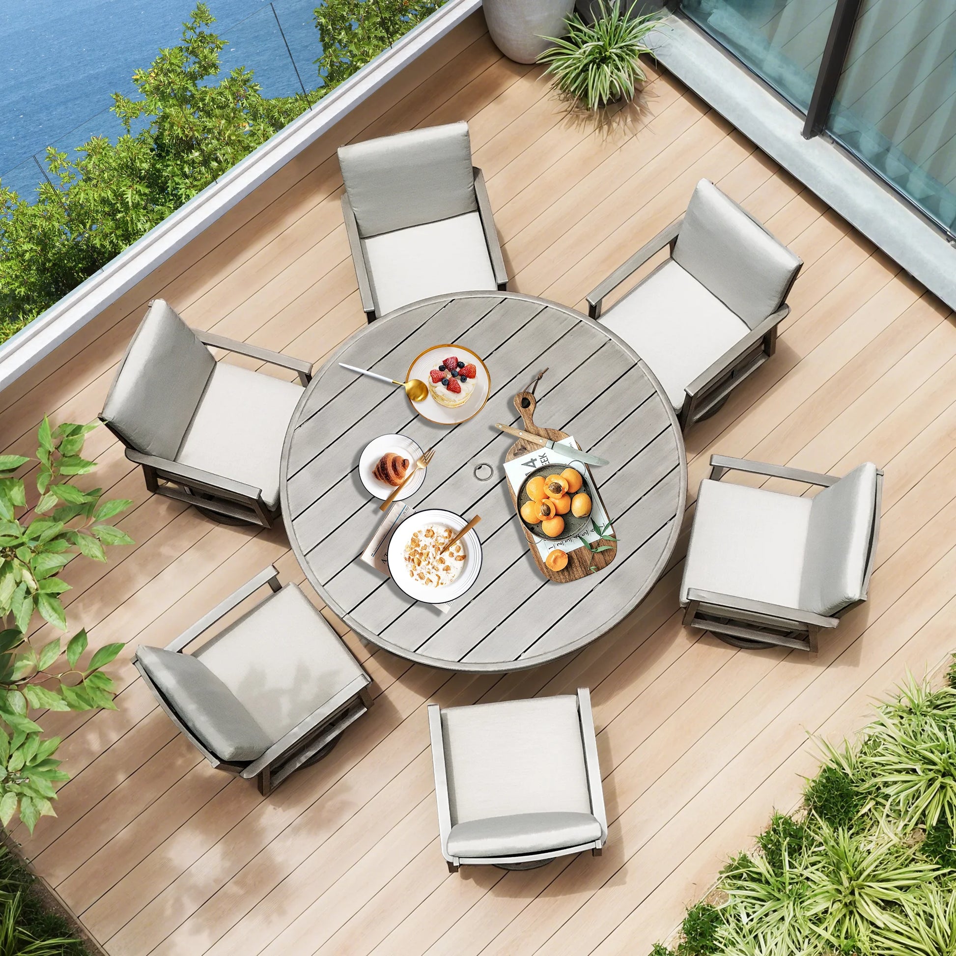 Outdoor patio set with a round table and chairs on a wooden deck by a body of water.