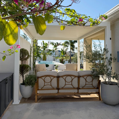 Outdoor patio with a wicker sofa, cushions, and potted plants on a sunny day.