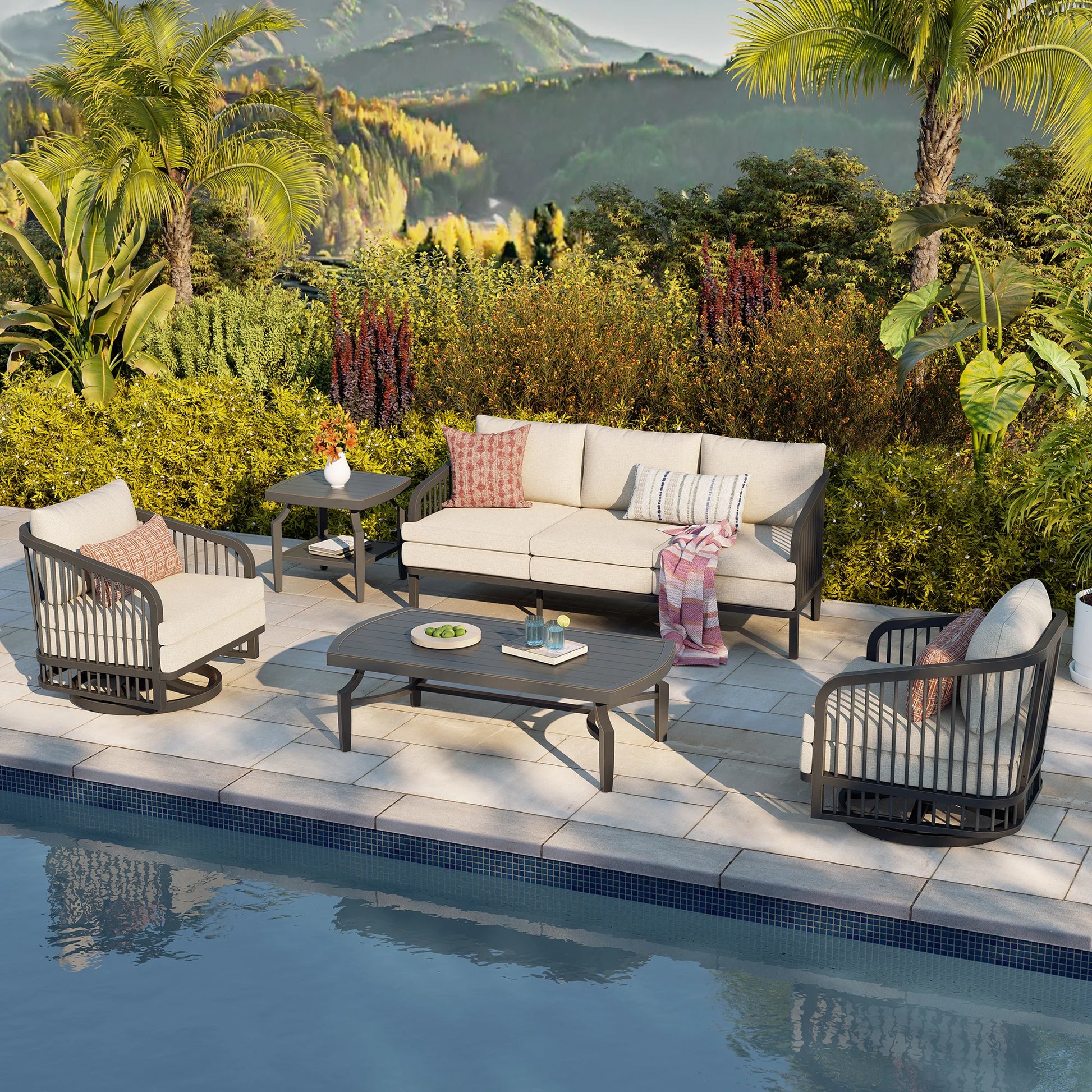 Outdoor patio set with furniture by a poolside, surrounded by greenery and mountains.