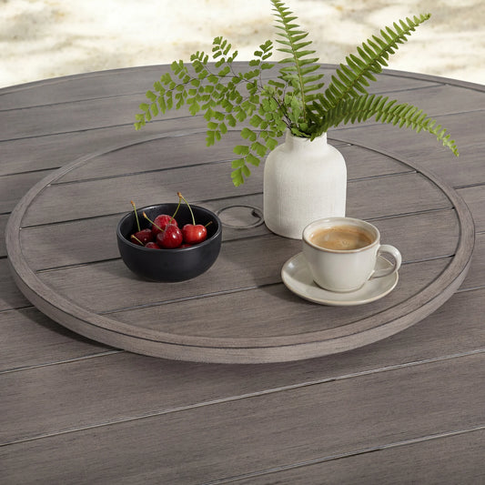 Round wooden table with a cup of coffee, bowl of cherries, and vase with ferns on a wooden floor.