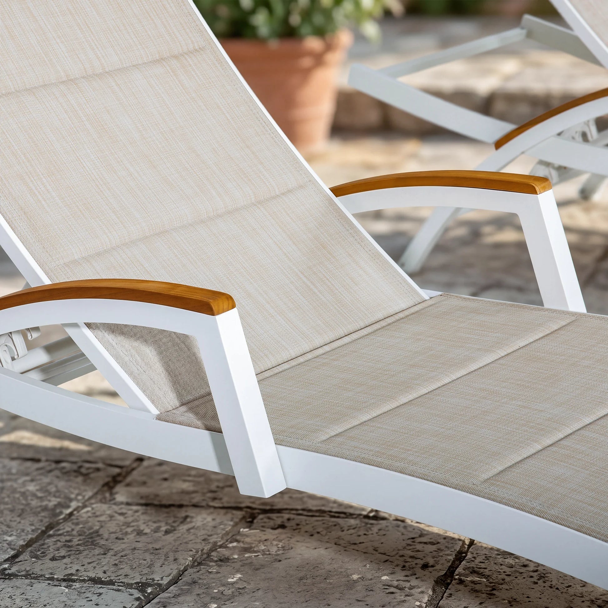 Beige lounge chair with wooden armrests on a stone patio