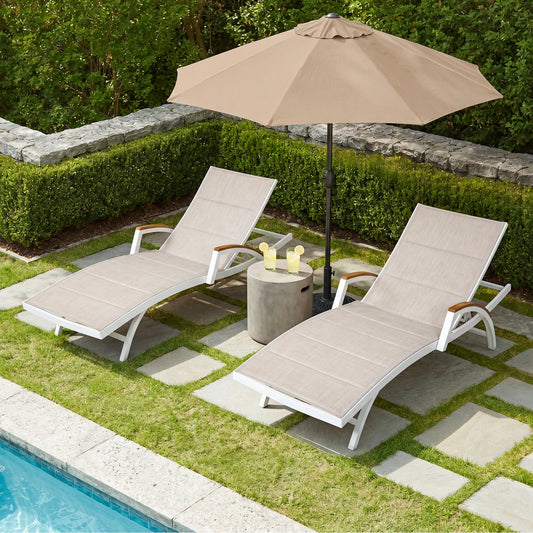 Two lounge chairs with a beige umbrella and small table by a poolside.