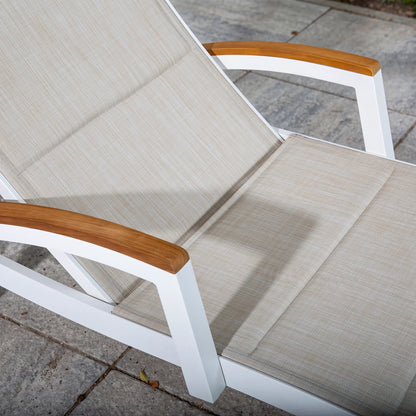 White lounge chair with beige cushions and wooden armrests on a stone patio.