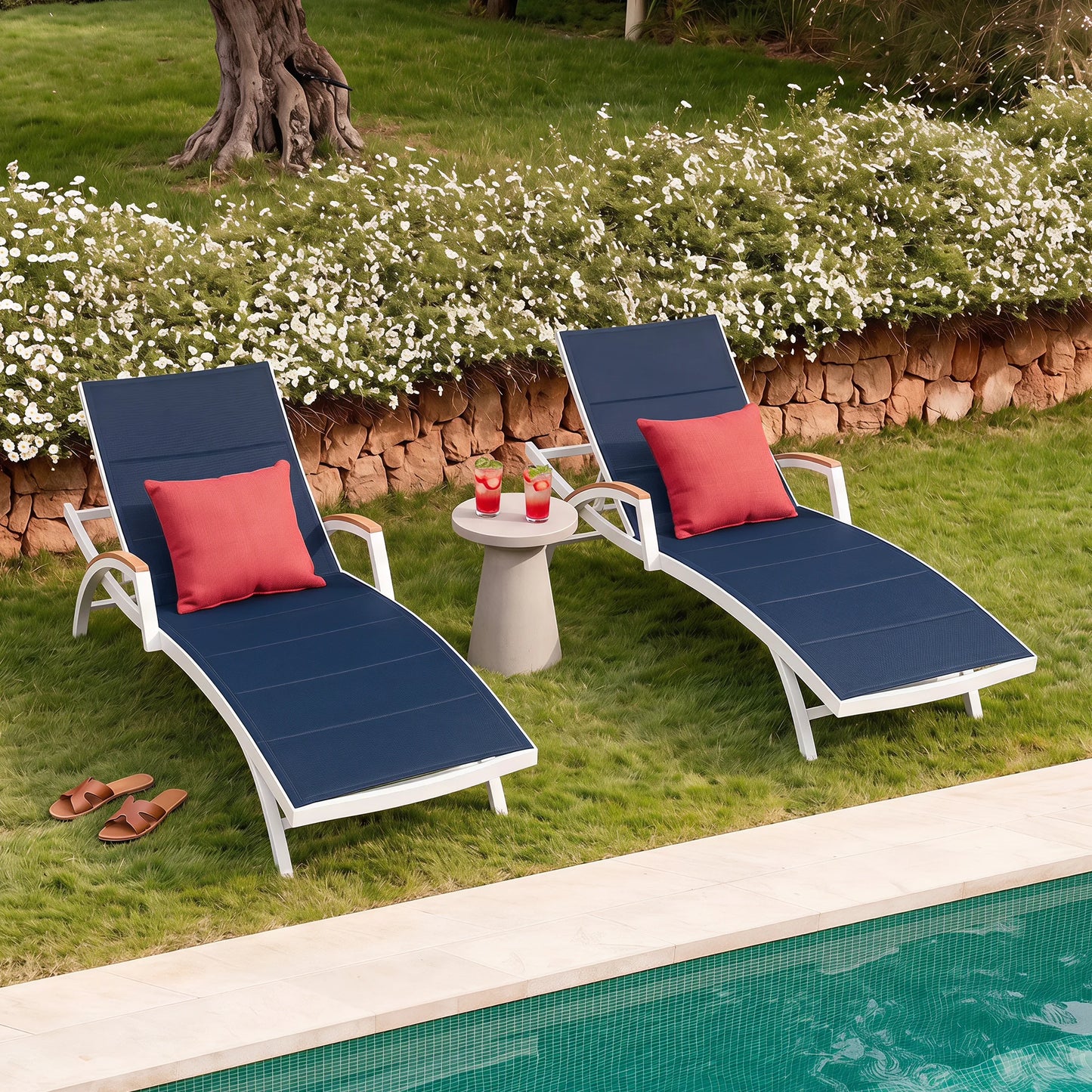 Two blue lounge chairs with red cushions by a poolside on a grassy area with flowers.