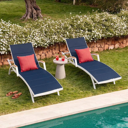 Two blue lounge chairs with red cushions by a poolside on a grassy area with flowers.