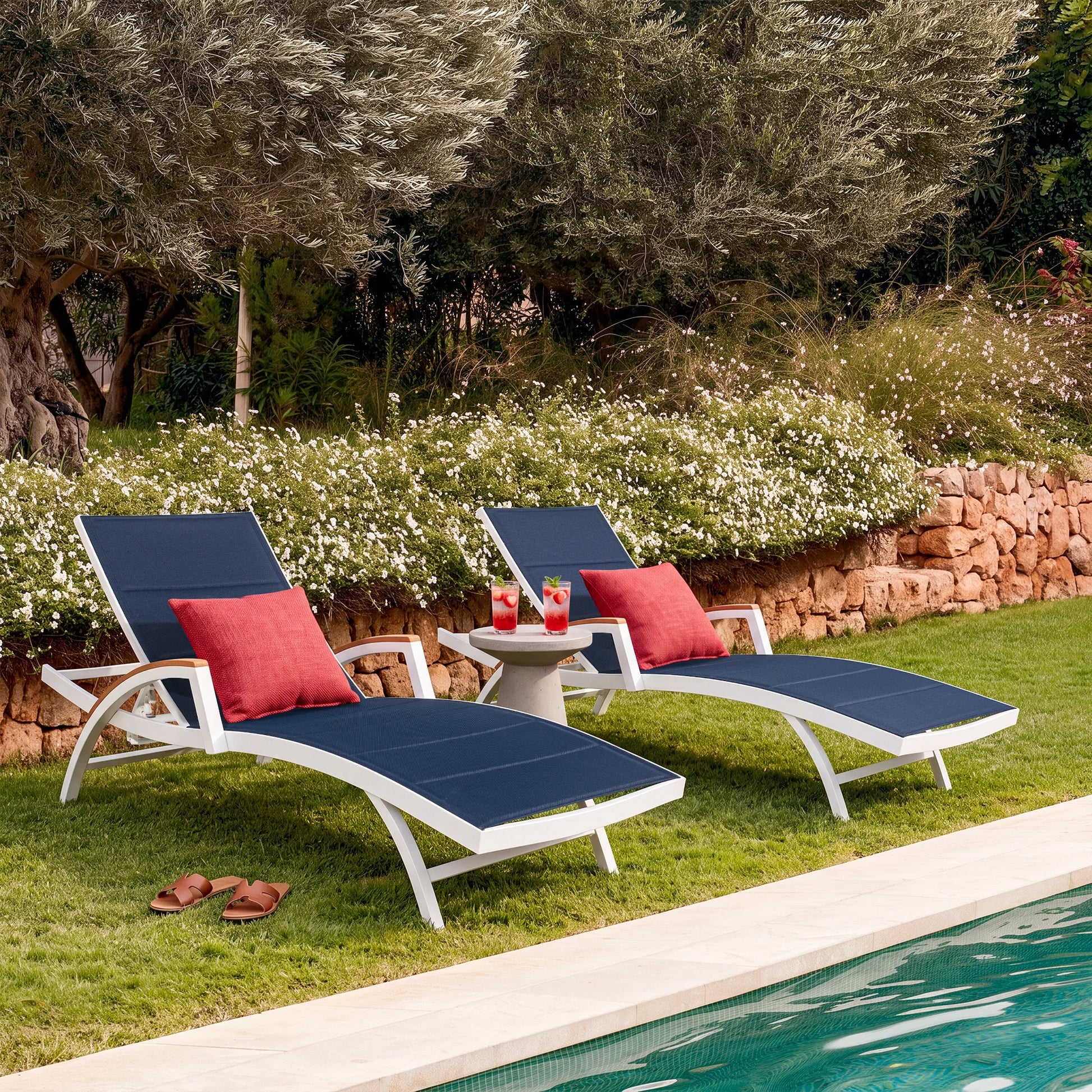 Two blue lounge chairs with red cushions by a poolside in a garden setting.