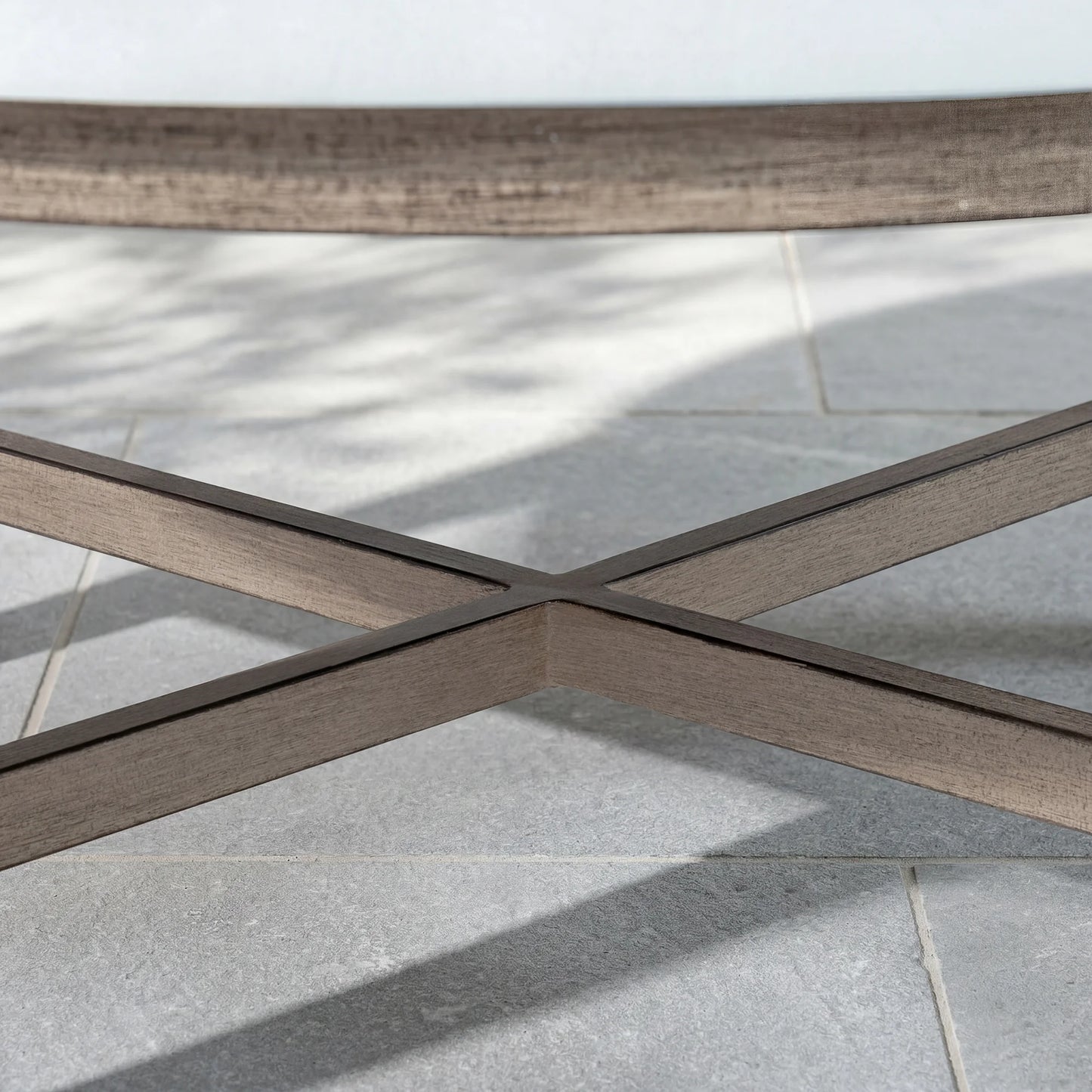 Close-up of a wood-look outdoor table with a cross-pattern on a tiled floor.