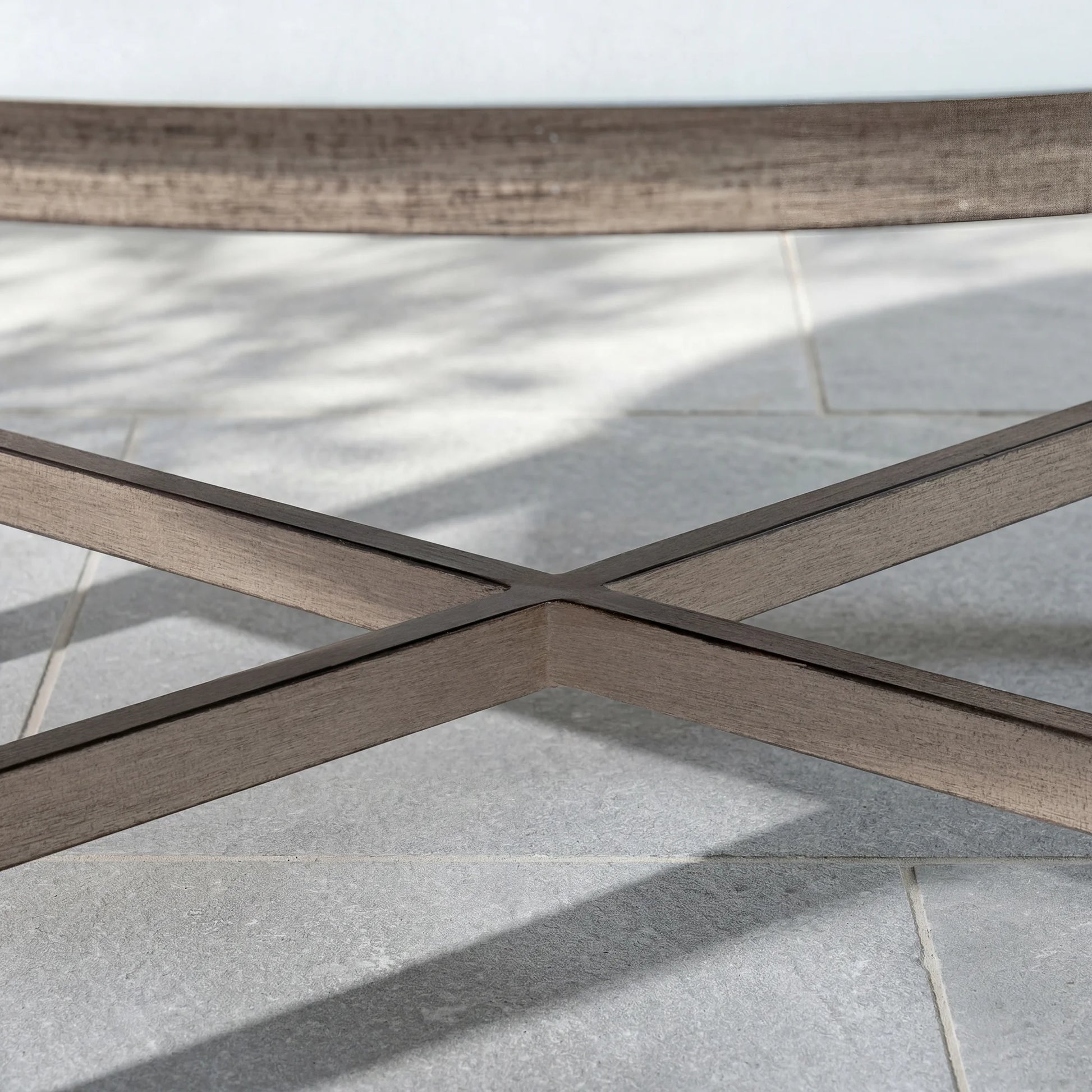 Close-up of a wood-look outdoor table with a cross-pattern on a tiled floor.