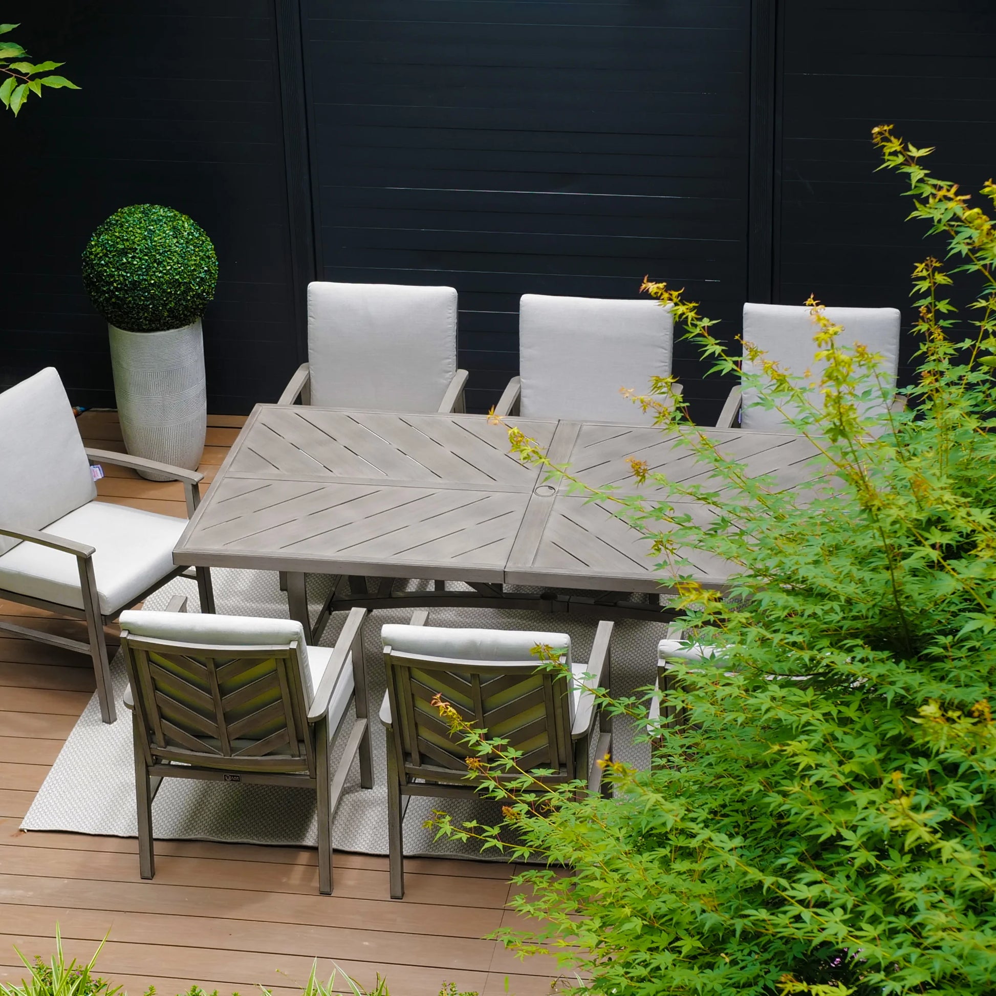 Outdoor patio set with a wooden table and chairs on a deck, surrounded by greenery.