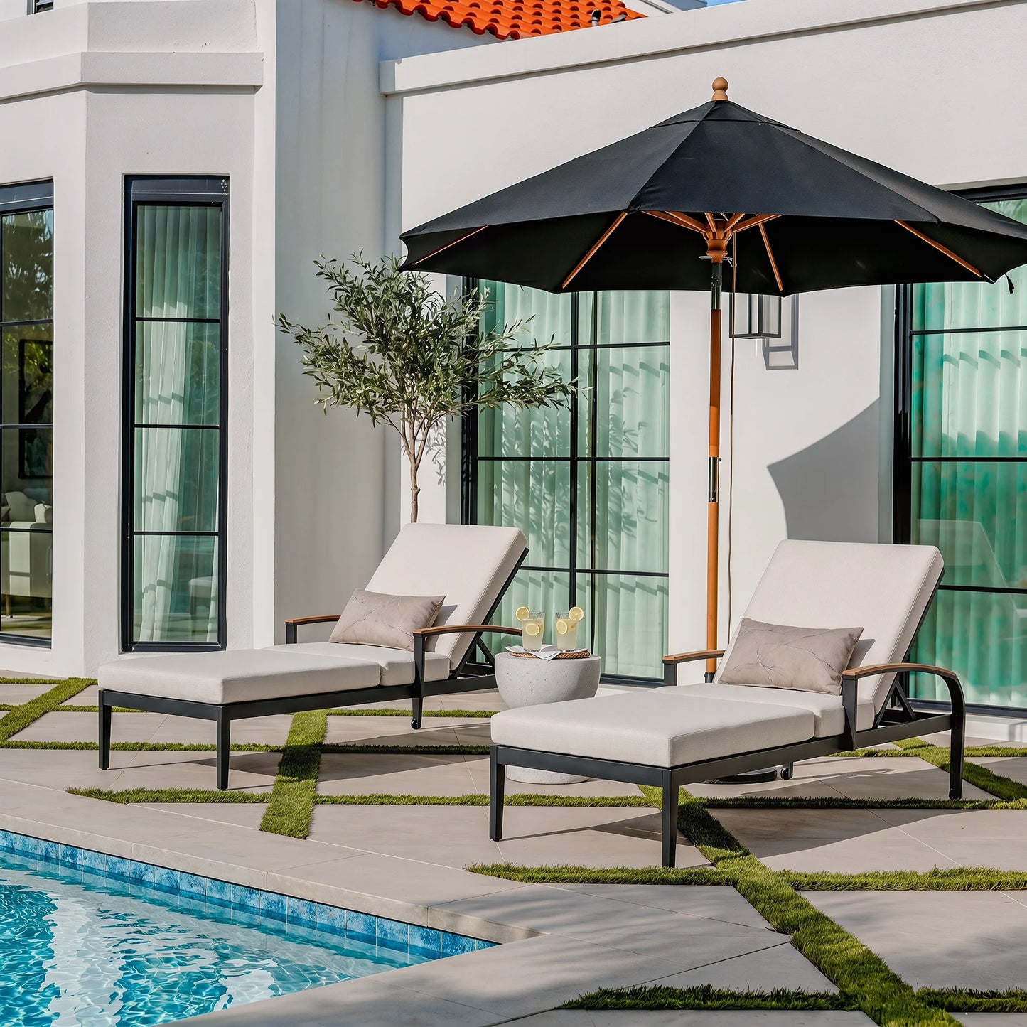 Two lounge chairs with a black umbrella by a poolside.