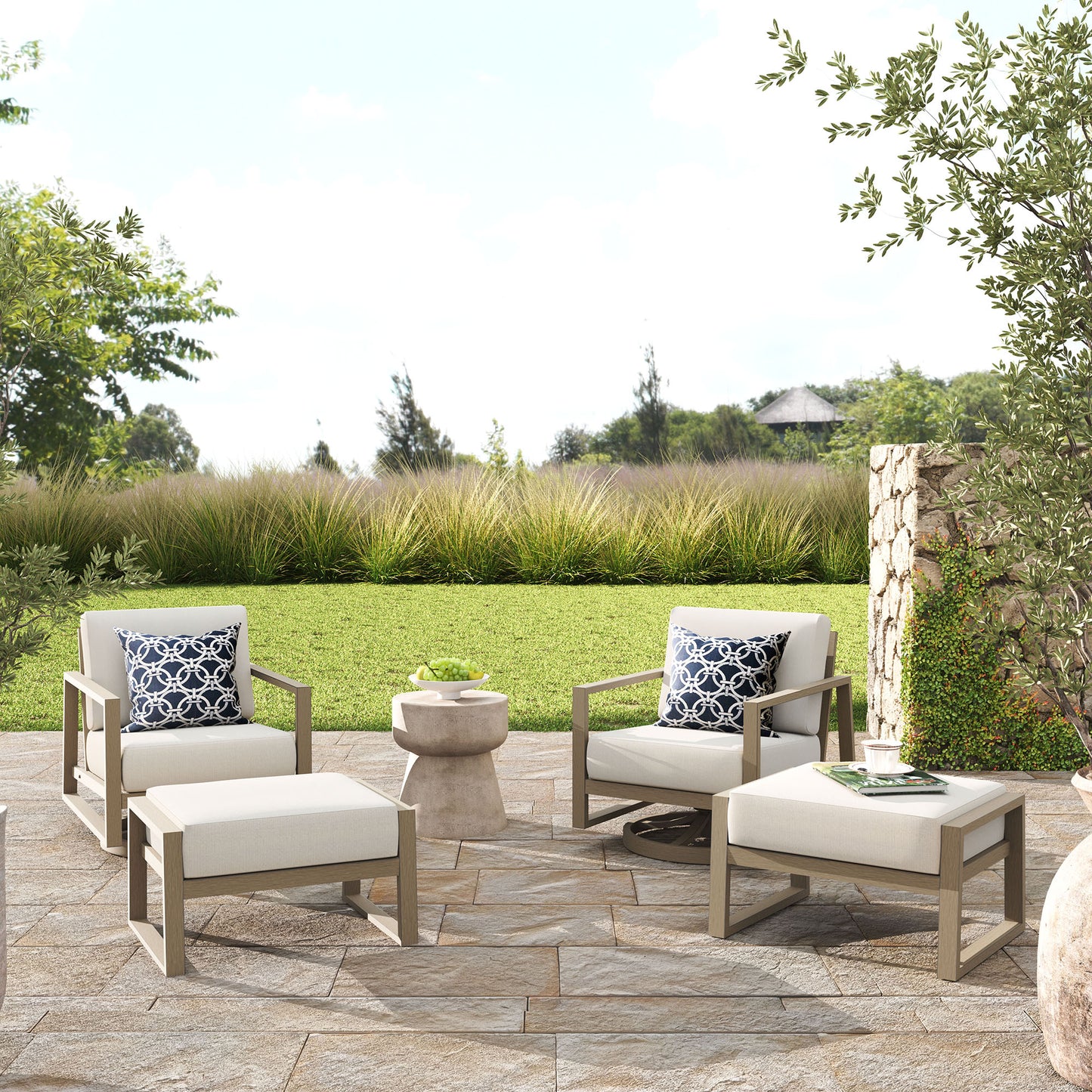 Outdoor patio furniture set with chairs, ottomans, and a table on a stone patio.
