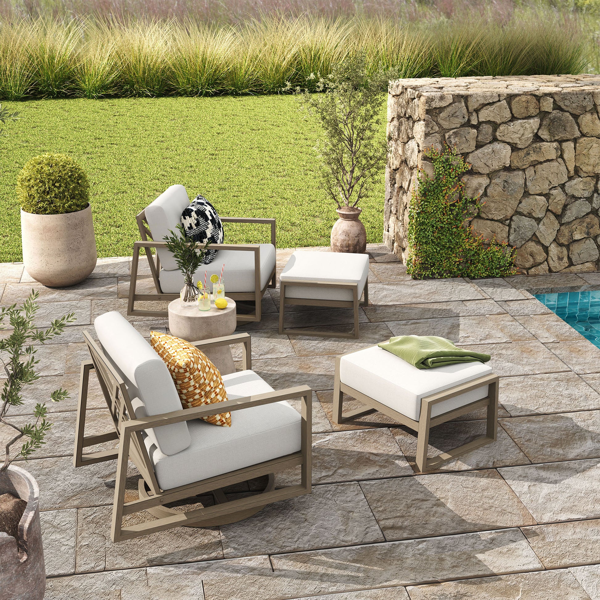 Outdoor patio set with chairs, table, and ottoman on a stone patio by a pool.