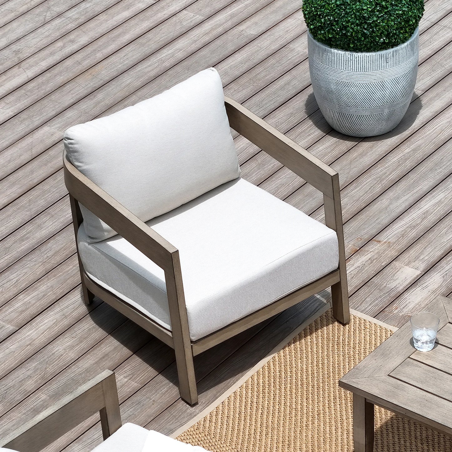 Wooden armchair with white cushions on a wooden deck with a potted plant.