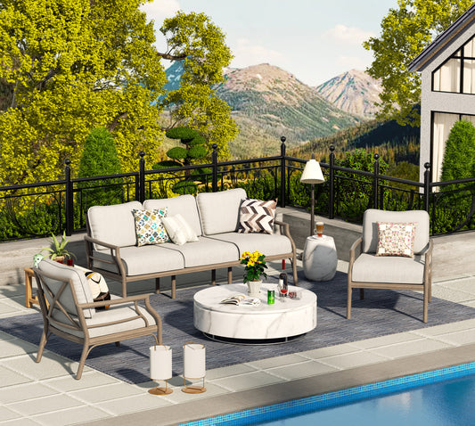 Outdoor patio seating set including a sofa and two chairs with beige cushions, placed on a tiled area next to a pool with a mountainous background.