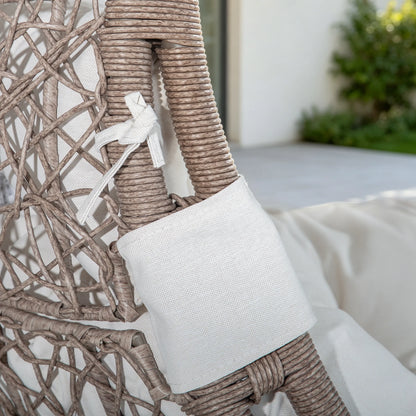 A close-up of a woven outdoor chair with a white fabric cushion and tie on the armrest, set in a patio environment.