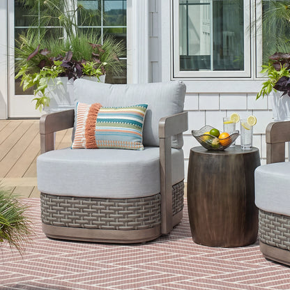 A single Manarola gray fixed club chair styled with a colorful accent pillow on a backyard deck next to a metallic side table.