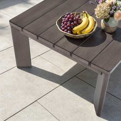 High-angle shot of the Manarola grey slatted coffee table topped with a fruit bowl containing bananas and grapes on a stone tiled patio.