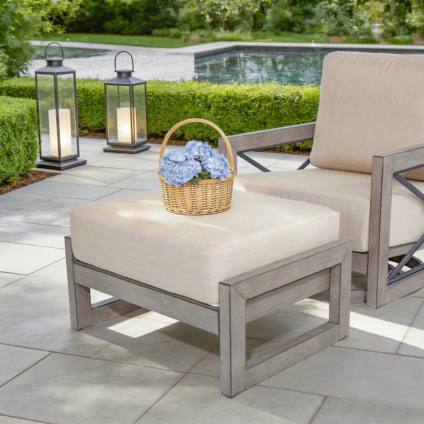 Outdoor patio set with ottoman, chair, and lanterns near a pool.