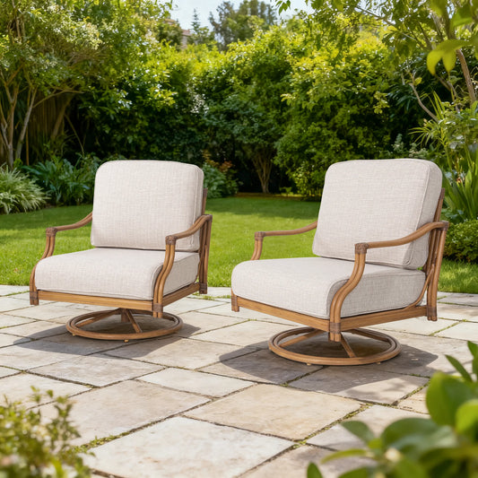 Two beige cushioned chairs with aluminum frames on a stone patio surrounded by greenery.