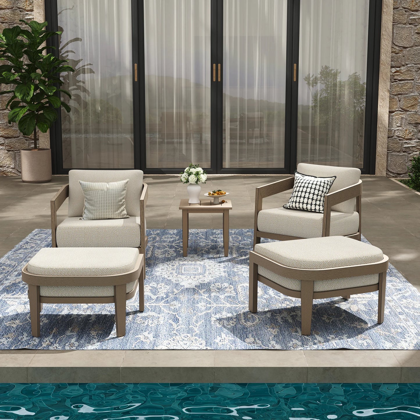 Outdoor patio set with chairs, ottoman, and table on a rug in front of a stone wall.