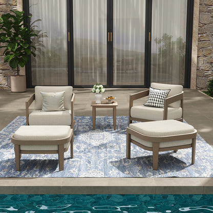 Outdoor patio set with chairs, ottoman, and table on a rug in front of a stone wall.