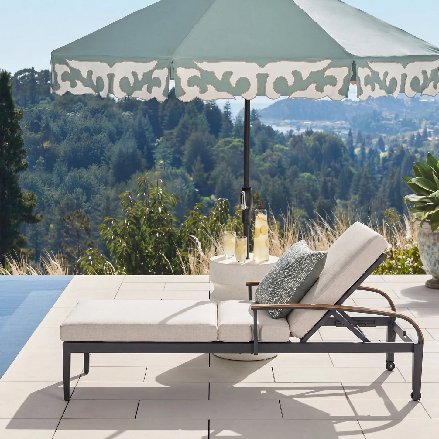 Outdoor lounge chair with umbrella and cushions on a patio with scenic view