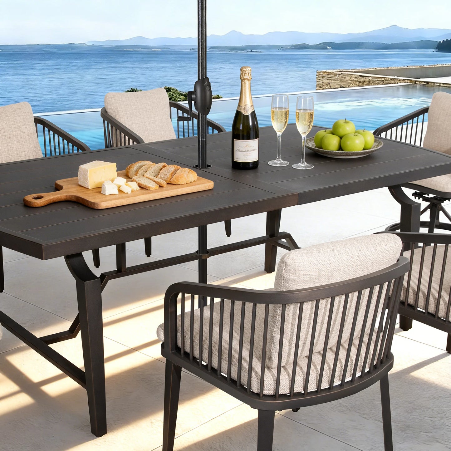 Outdoor dining table with chairs, wine, cheese, and bread on a patio with ocean view.