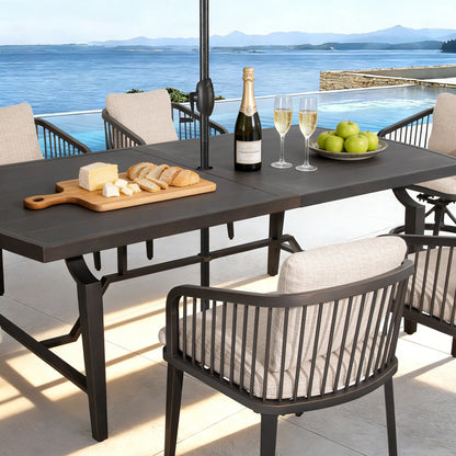 Outdoor dining table with chairs, wine, cheese, and bread on a patio with ocean view.