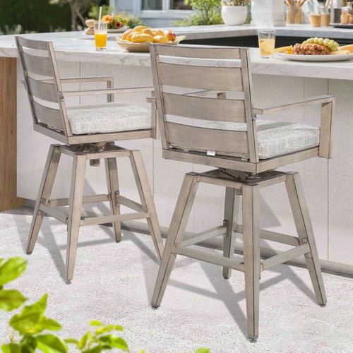 Two wooden bar stools with gray cushions on a patio with a table and food in the background.